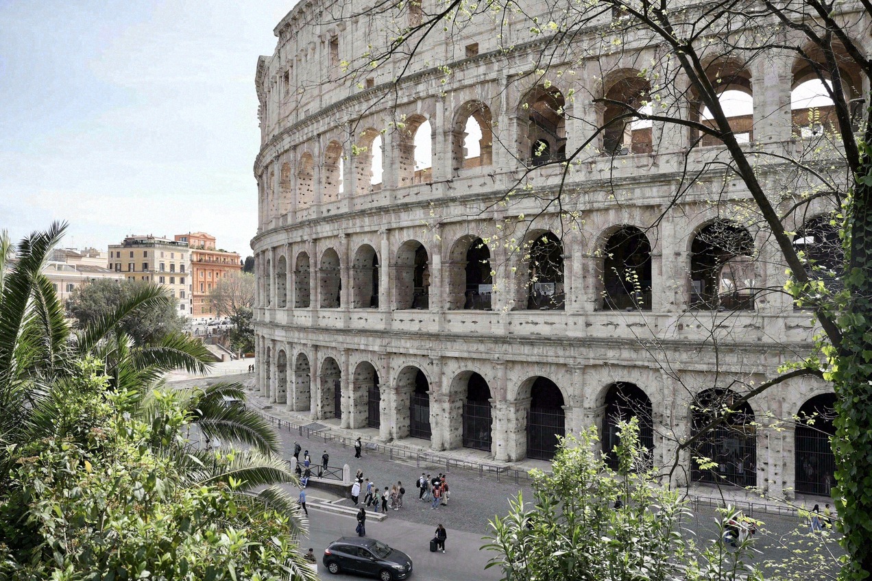 The Colosseum in Rome seen from the street, with the arches of the outer wall and visitors in front.